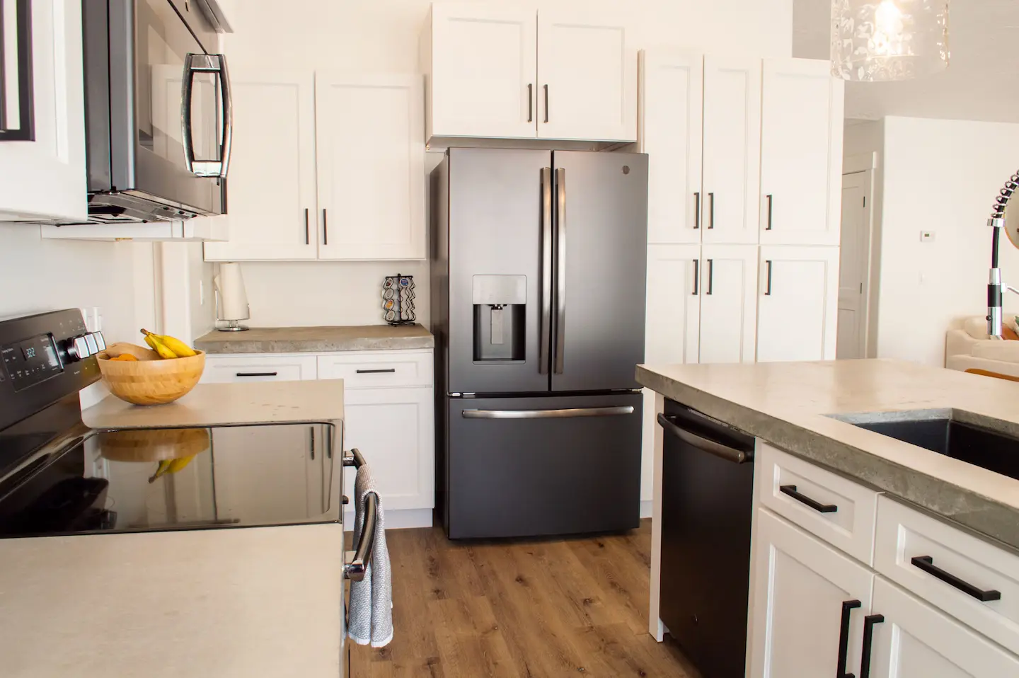 Kitchen remodel with white shaker cabinets, concrete countertops, black-stainless French-door fridge, island, and wood floors.