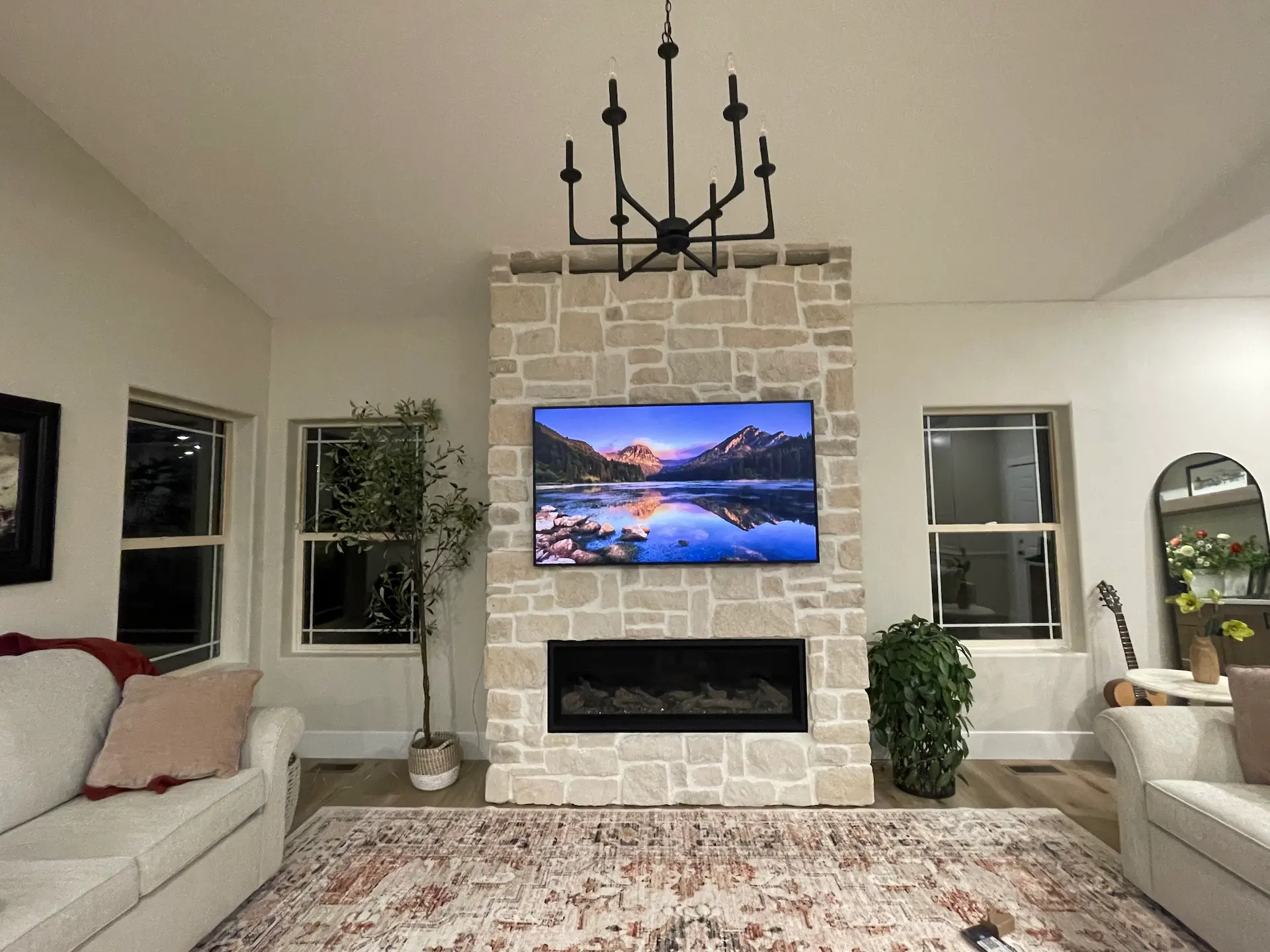 Living room remodel with stacked-stone fireplace and mounted TV, updated lighting and finishes.